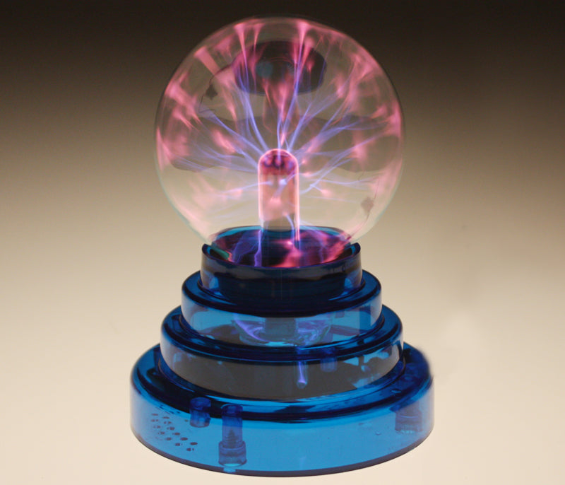 The Genius at Play Electric Eel Plasma Ball features pink and purple electric streams from a central electrode in a clear glass sphere atop a blue tiered base, all set against a softly glowing warm beige background.