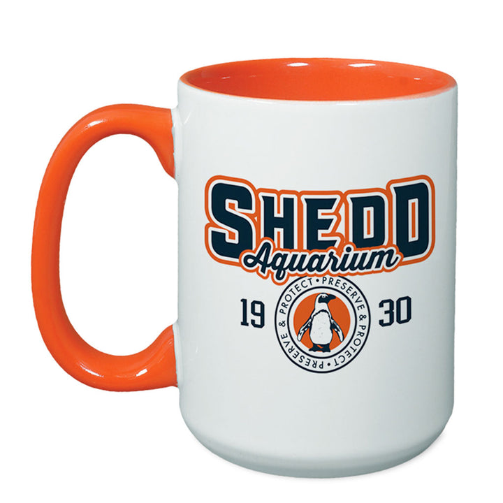 The Shedd Aquarium Sporty Two-Tone Mug features a white exterior, orange interior and handle, bold mug lettering, "1930," and a collegiate-style circular logo with a penguin and "Protect, Preserve & Protect.
