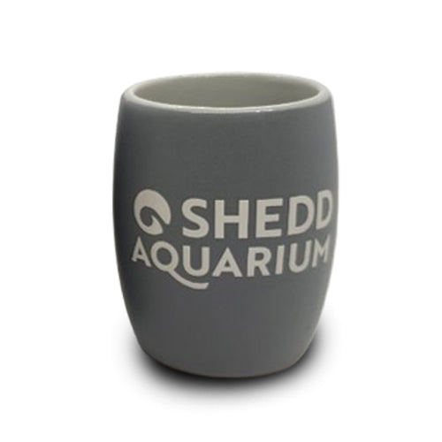 A clear shot glass etched with “Shedd Aquarium” on the front and featuring a beluga design, celebrating aquatic conservation, displayed against a plain white background.