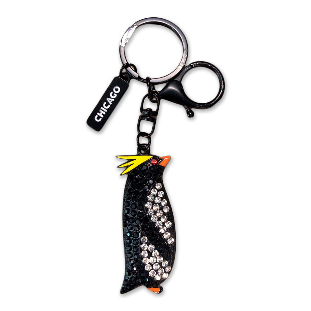 The Shedd Aquarium Rock Hopper Penguin Bling Keychain features a black and white penguin charm with yellow tufts, an orange beak, sparkling rhinestones, and a black CHICAGO tag—ideal for any Shedd Aquarium fan.