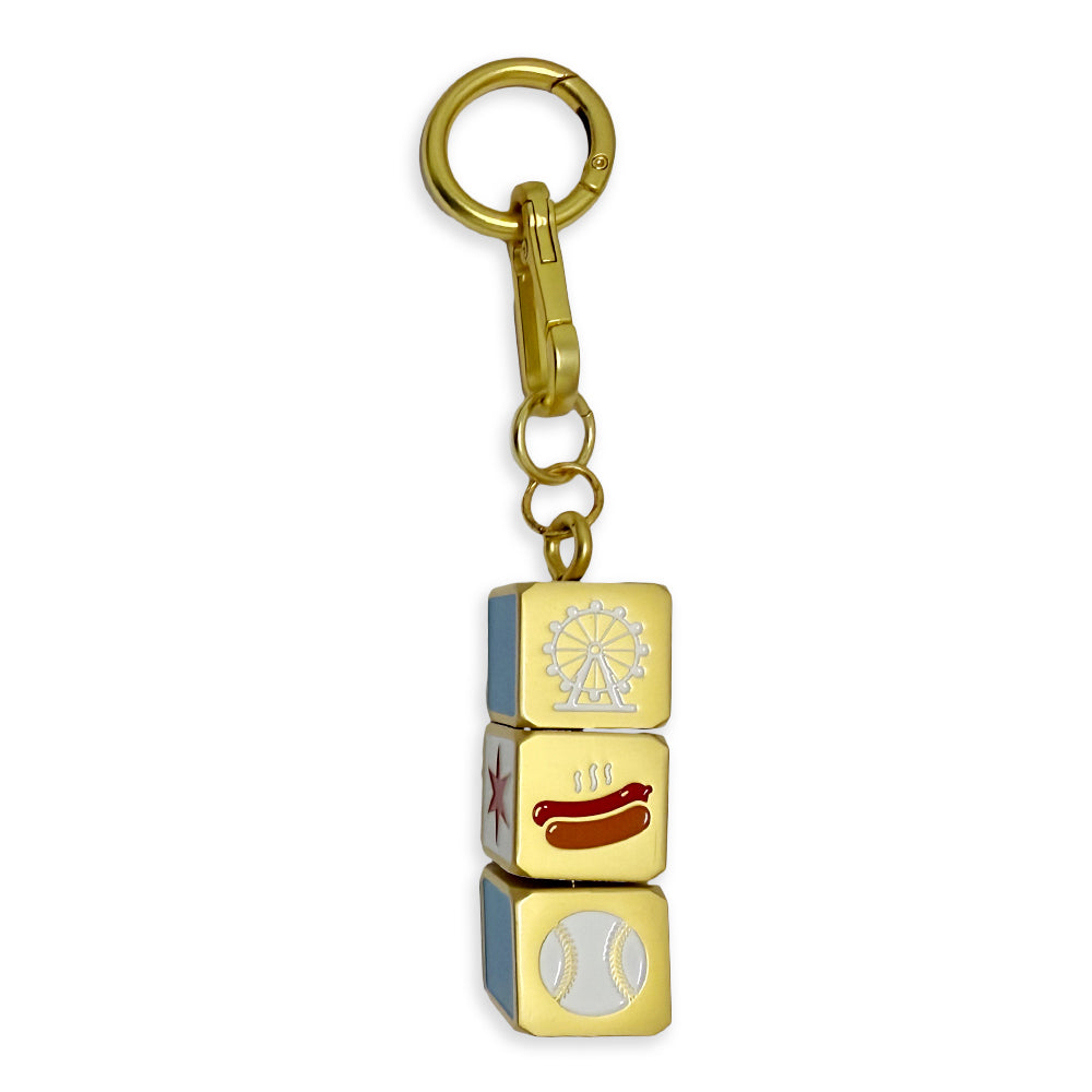 The Chicago Block Spinner Bag Charm features a gold keychain with three stacked cubes, each displaying a unique design—a Ferris wheel, a hot dog, and a baseball—making it an ideal playful yet iconic Chicago accessory for your bag or collection.