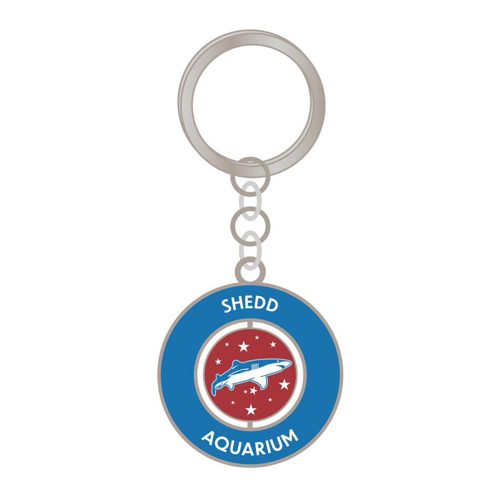 The Shedd Aquarium Red White & Ocean Blue Spinner Keychain features a blue border, "Shedd Aquarium" in white text, and a center with a white and blue whale plus stars on red—ideal for ocean conservation fans.