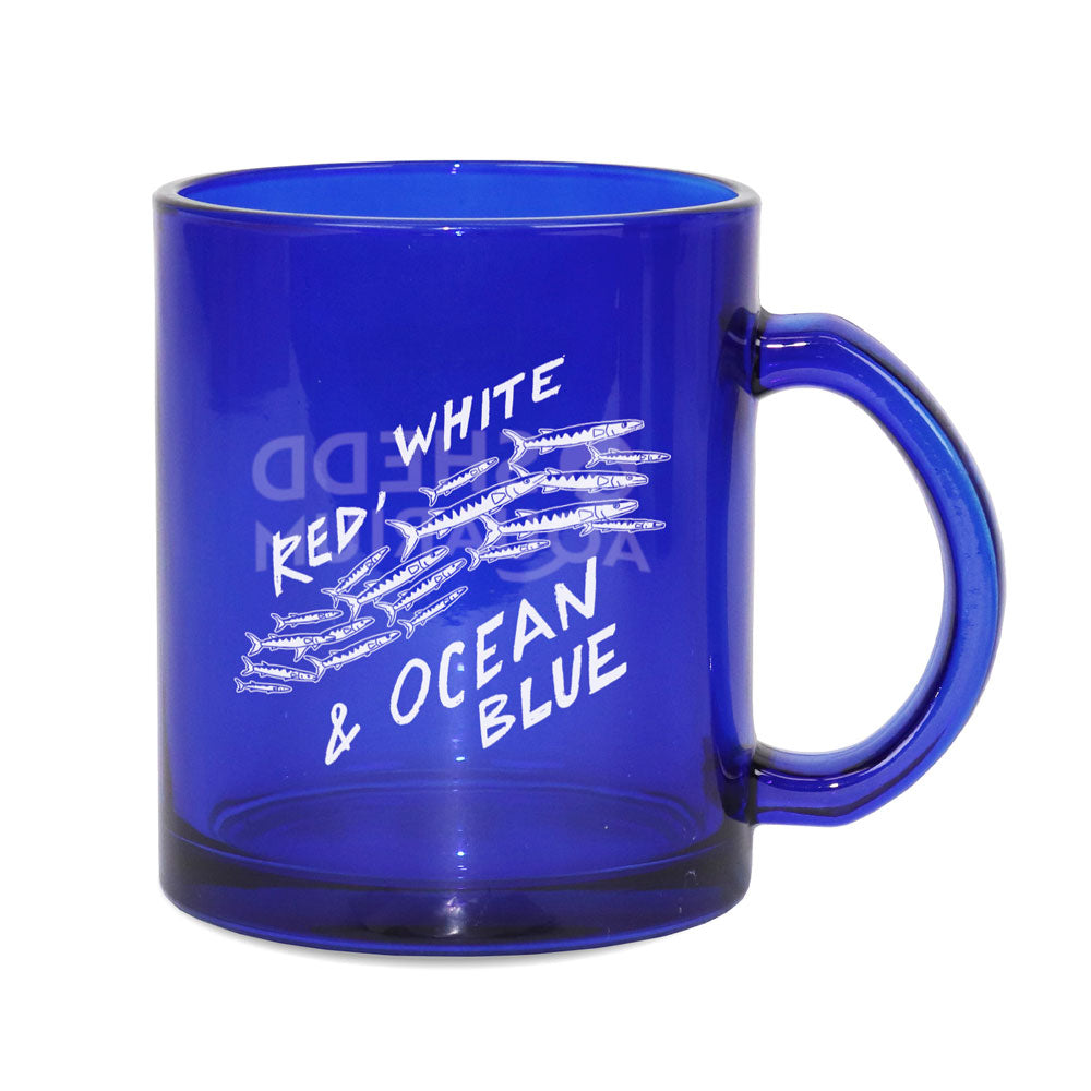 The Shedd Aquarium Red White & Ocean Blue Mug is a translucent blue glass mug with a handle, decorated with white text and graphics of small marine life and fish.