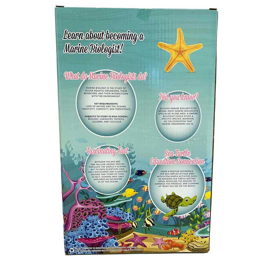 The back of the Marine Biologist Doll - Dk. Blonde box displays vibrant ocean art with fish, coral, a sea turtle, and starfish. Text shares what marine biologists do plus fun facts about marine life and sustainability.