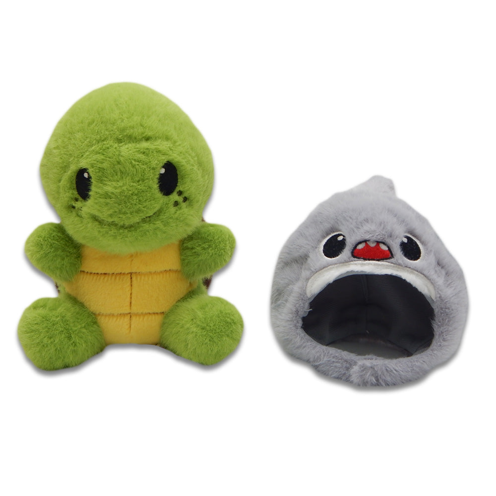 The Sea Turtle with Shark Cap Cutie Plush features a soft green turtle with a yellow belly and a removable shark cap, complete with red mouth and white teeth, designed to fit over the turtle. This adorable duo is shown against a white background.