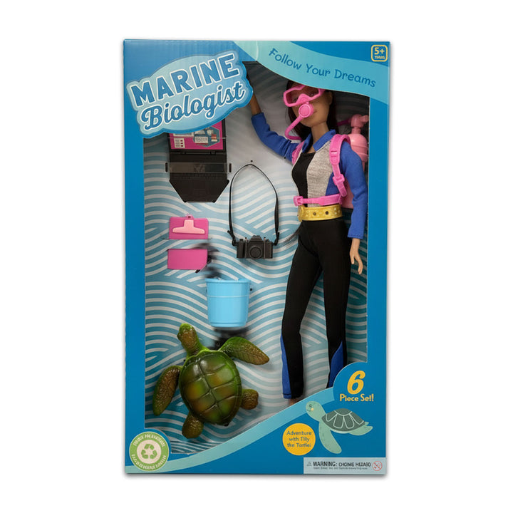 The Marine Biologist Doll - Dk. Blonde playset includes a doll in wetsuit, pink snorkel, blue tank, camera, pink cases, blue bucket, and green sea turtle. Box reads “Marine Biologist” and “Follow Your Dreams.” Promotes sustainability.