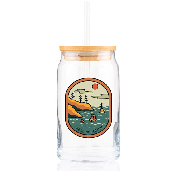 The Outdoorsy Otter Glass Tumbler is a clear glass water bottle with bamboo lid and straw, featuring a colorful otter swimming among trees, hills, sun, and clouds. “Shedd Aquarium” text appears at the bottom of the playful illustration.