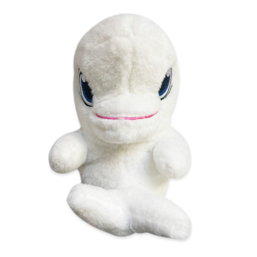 The Swaddle Babies Beluga Plush is a white plush toy shaped like a Beluga whale, featuring blue and black embroidered eyes and a small pink smile, shown sitting upright against a plain white background.